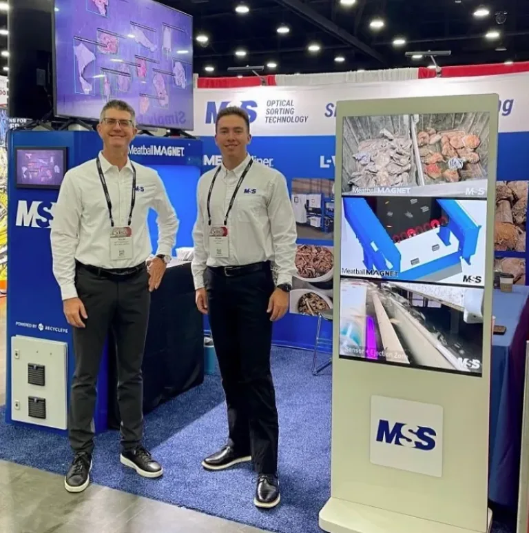 Two MSS employees standing in front of their tradeshow booth next to a digital kiosk