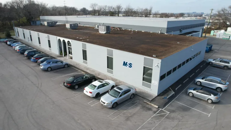 The updated MSS exterior drone image of the grey building with cars in the parking lot.