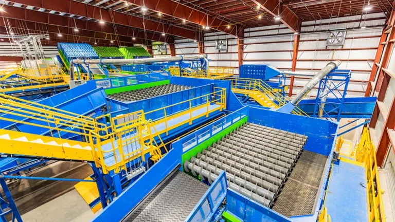 Interior view of a large recycling sorting facility with blue and yellow conveyor systems, roller screens, and chutes.