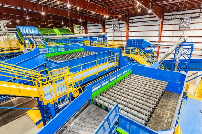 Interior view of a large recycling sorting facility with blue and yellow conveyor systems, roller screens, and chutes.